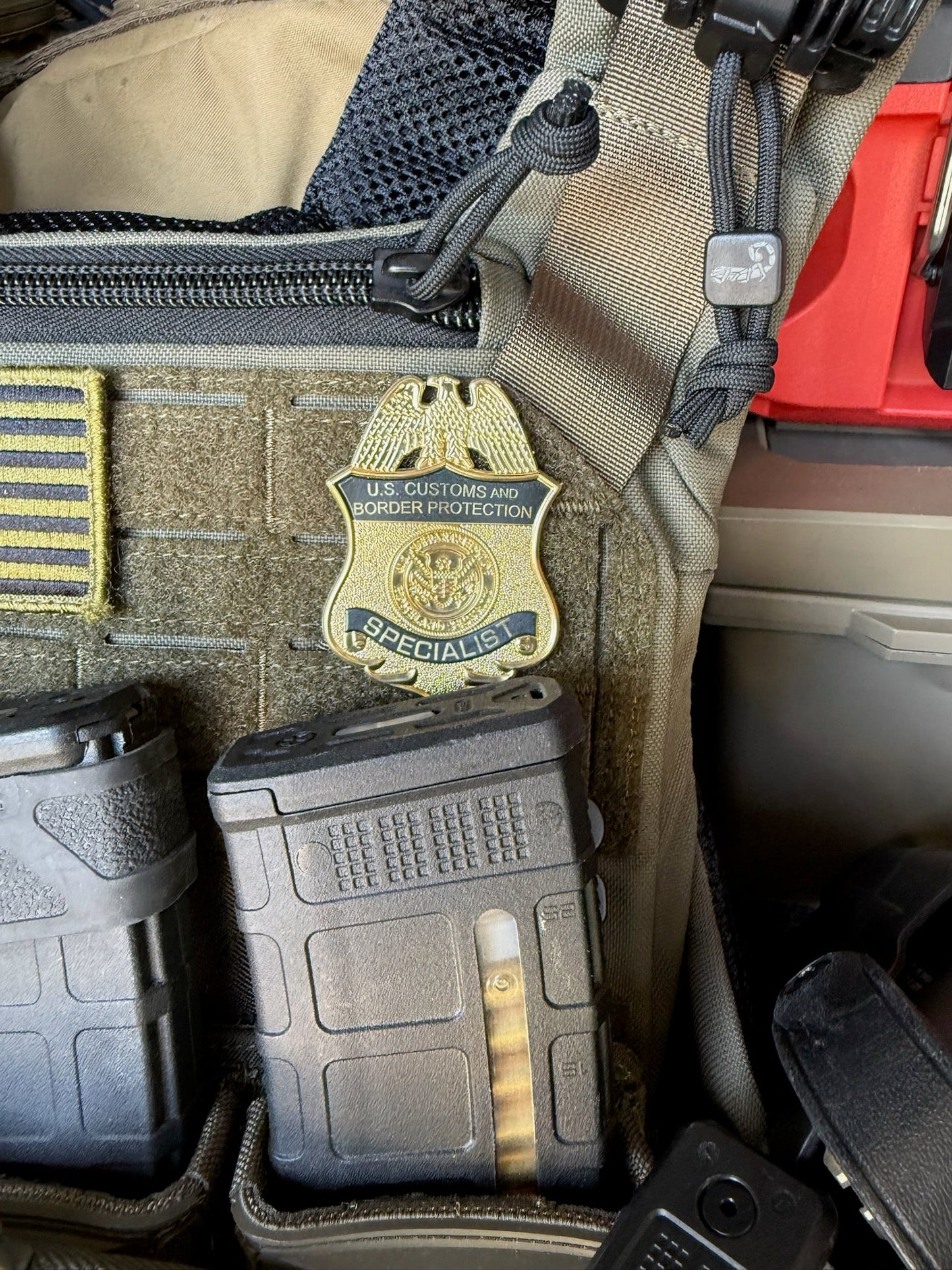 US Customs and Border Protection Specialist flex badge on tactical gear with various equipment.
