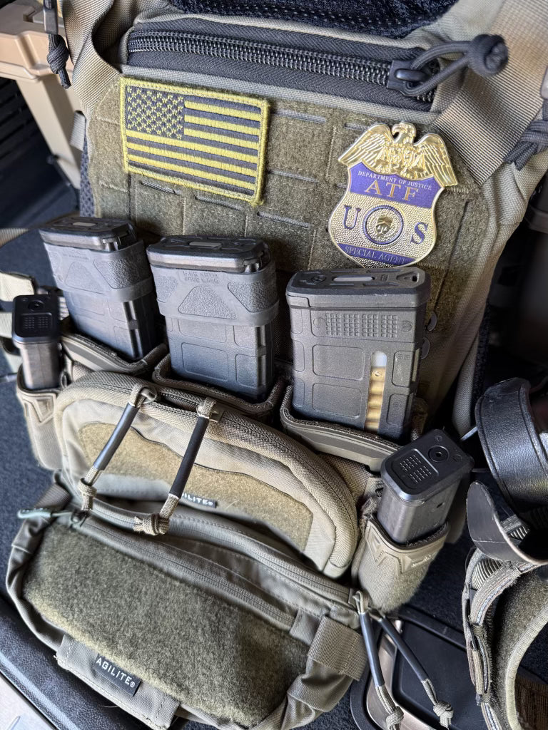 Close-up of tactical gear with American flag patch and ATF flex shield badge on a dark surface