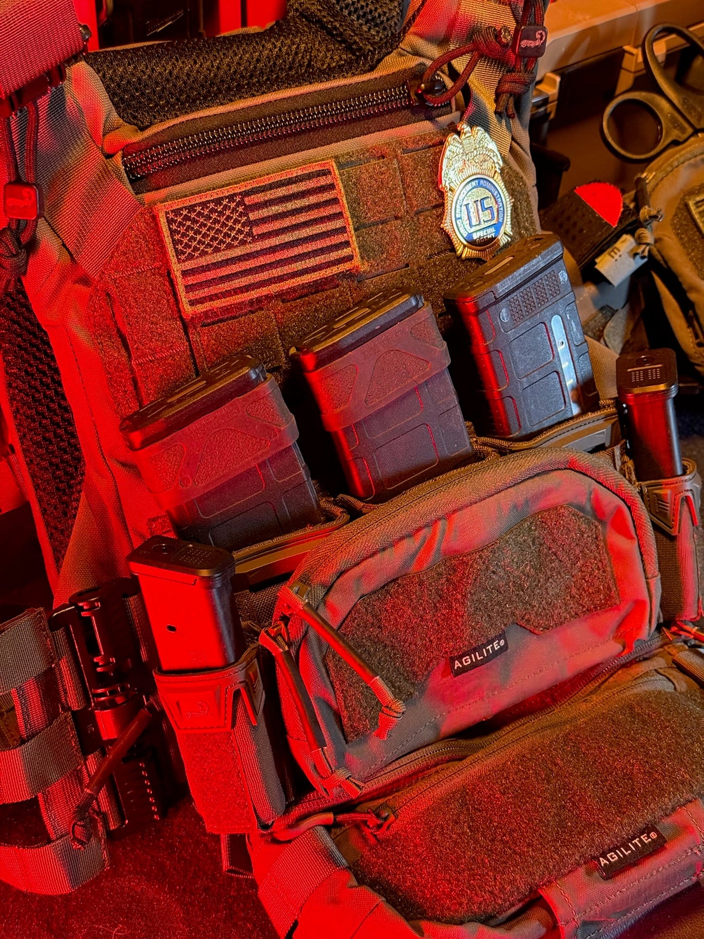Close-up of tactical gear with American flag patch and flexbadge, illuminated by red light.