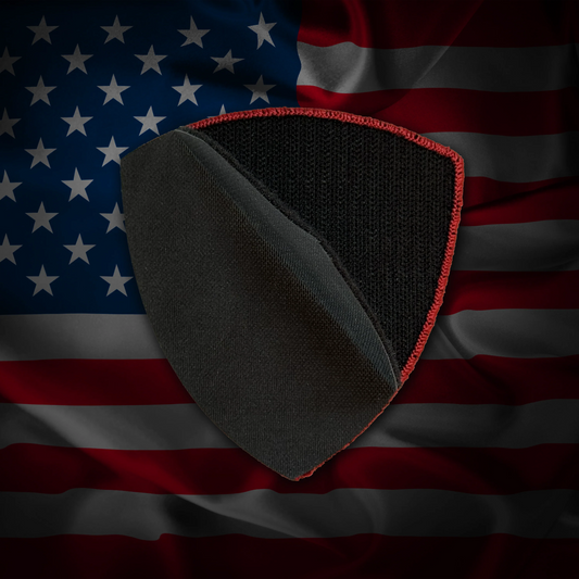 Black and red shield-shaped patch on an American flag background showing off the velcro backing of the patch.