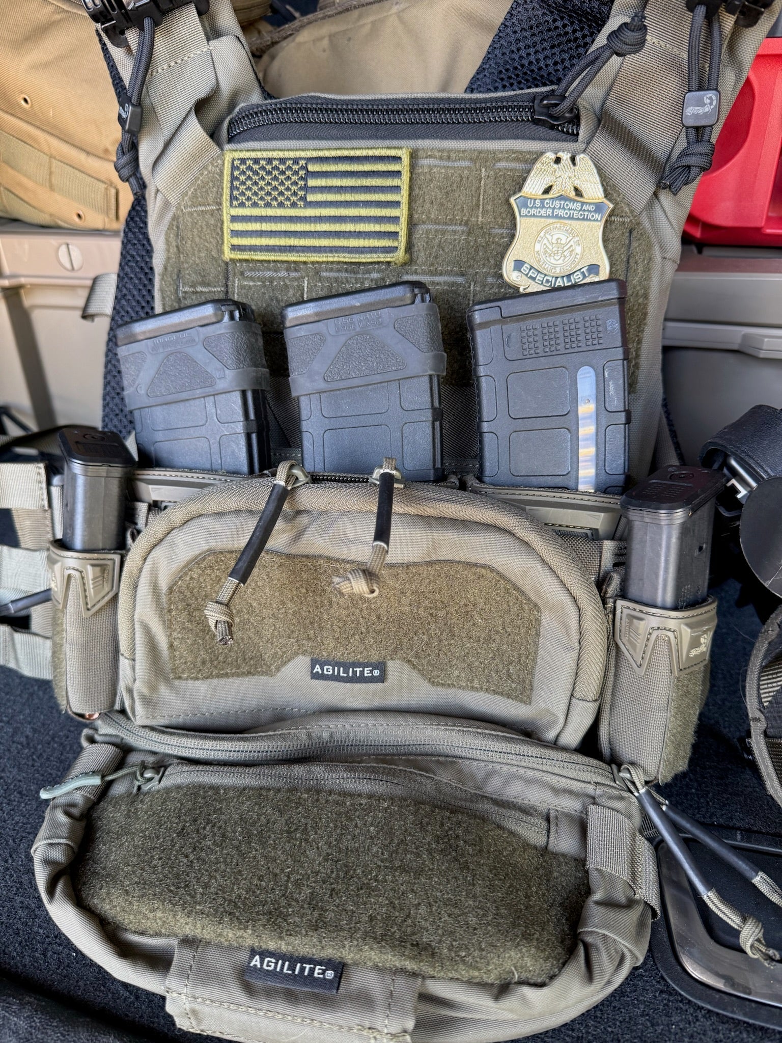 Close-up of a tactical vest with a CBP Flex Badge  with American flag patch and 'Agilite' branding.