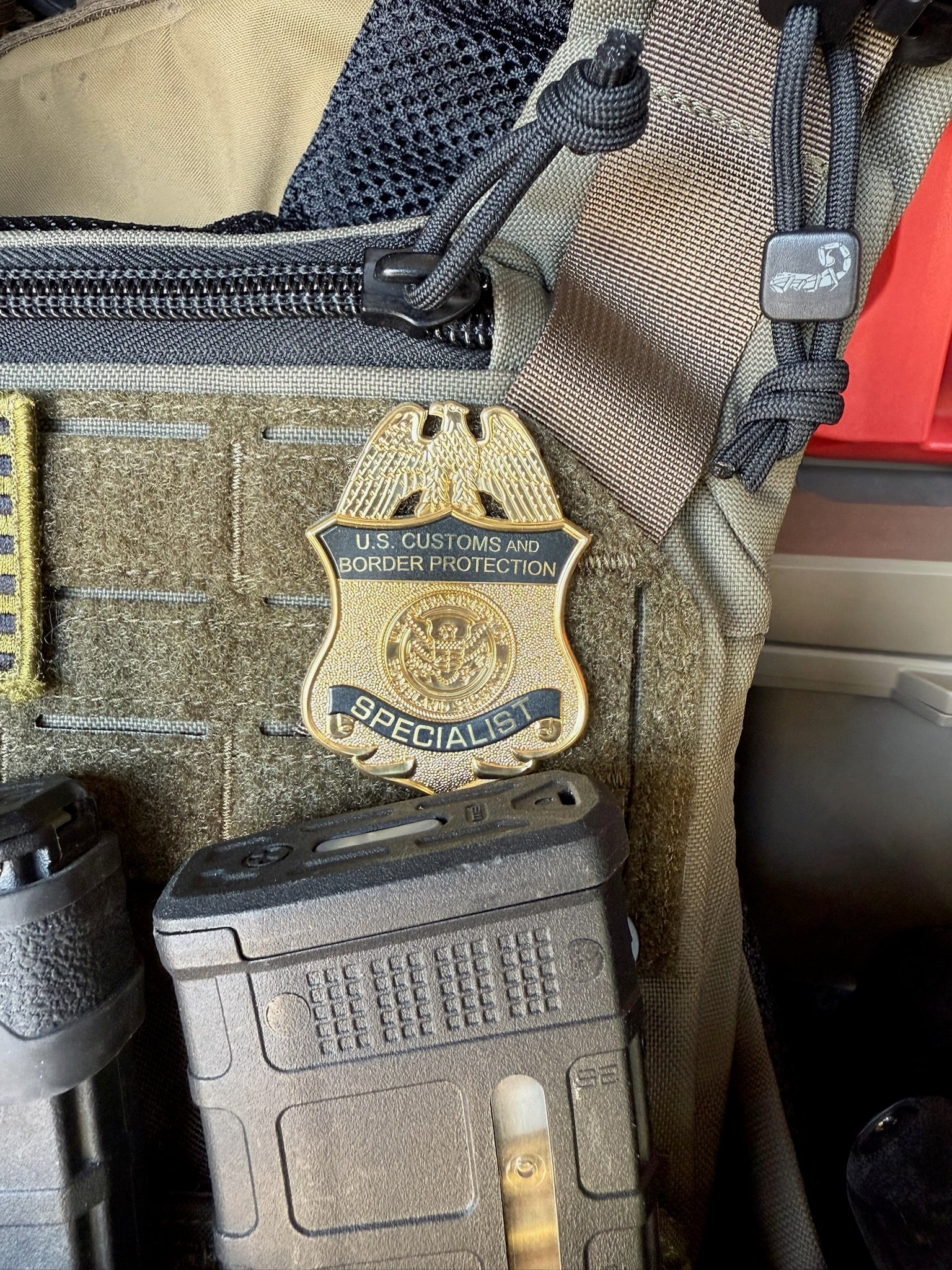 U.S. Customs and Border Protection Specialist flex shield badge on a tactical pouch with binoculars and other gear.