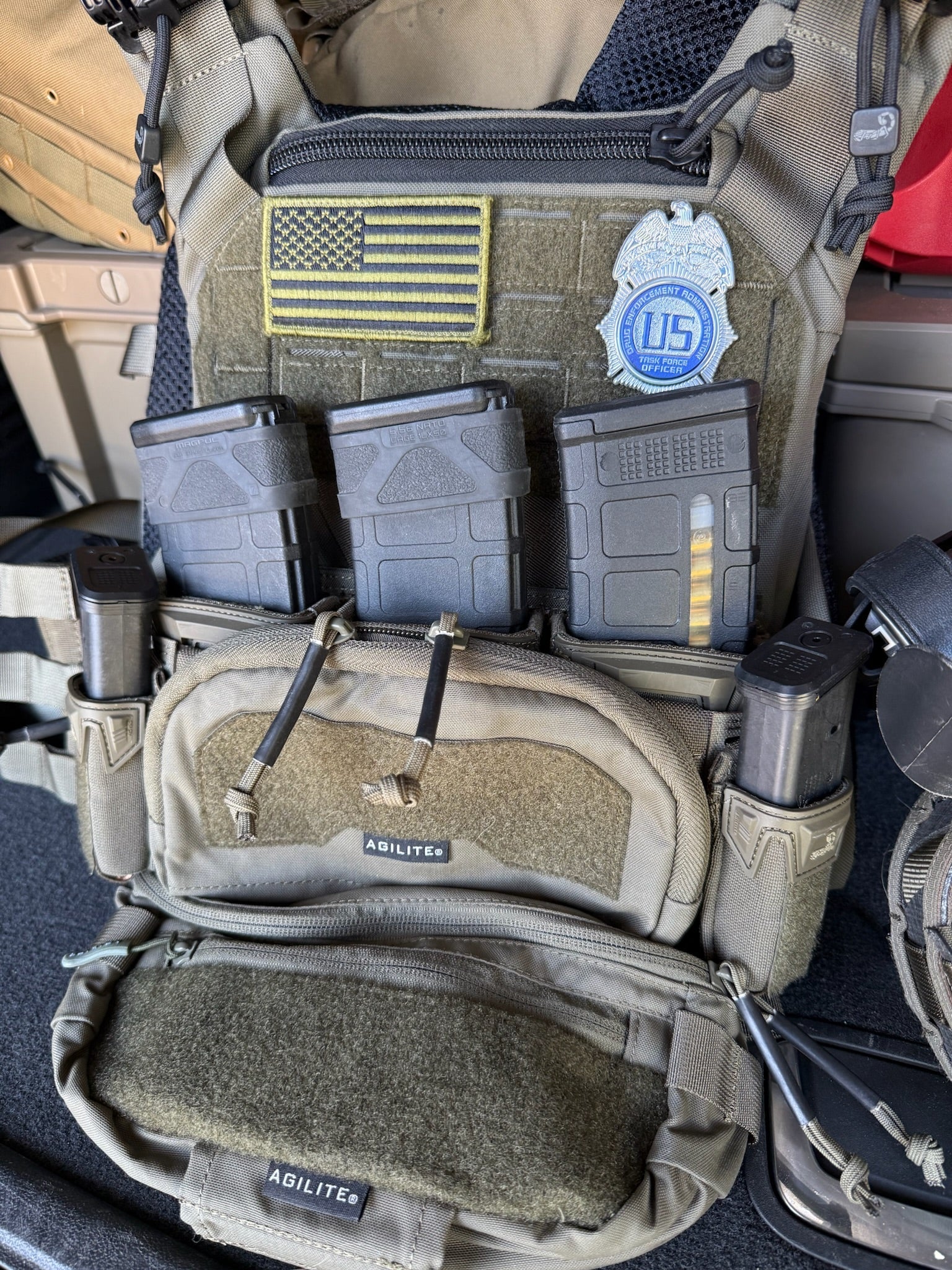 Tactical vest with DEA flex badge patch and American flag patch inside a vehicle.