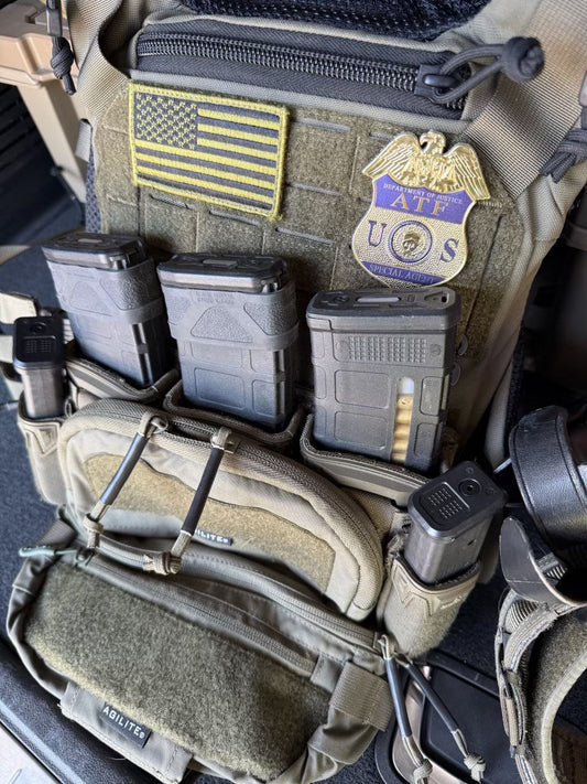 Close-up of tactical gear with American flag patch and ATF flex shield badge on a dark surface
