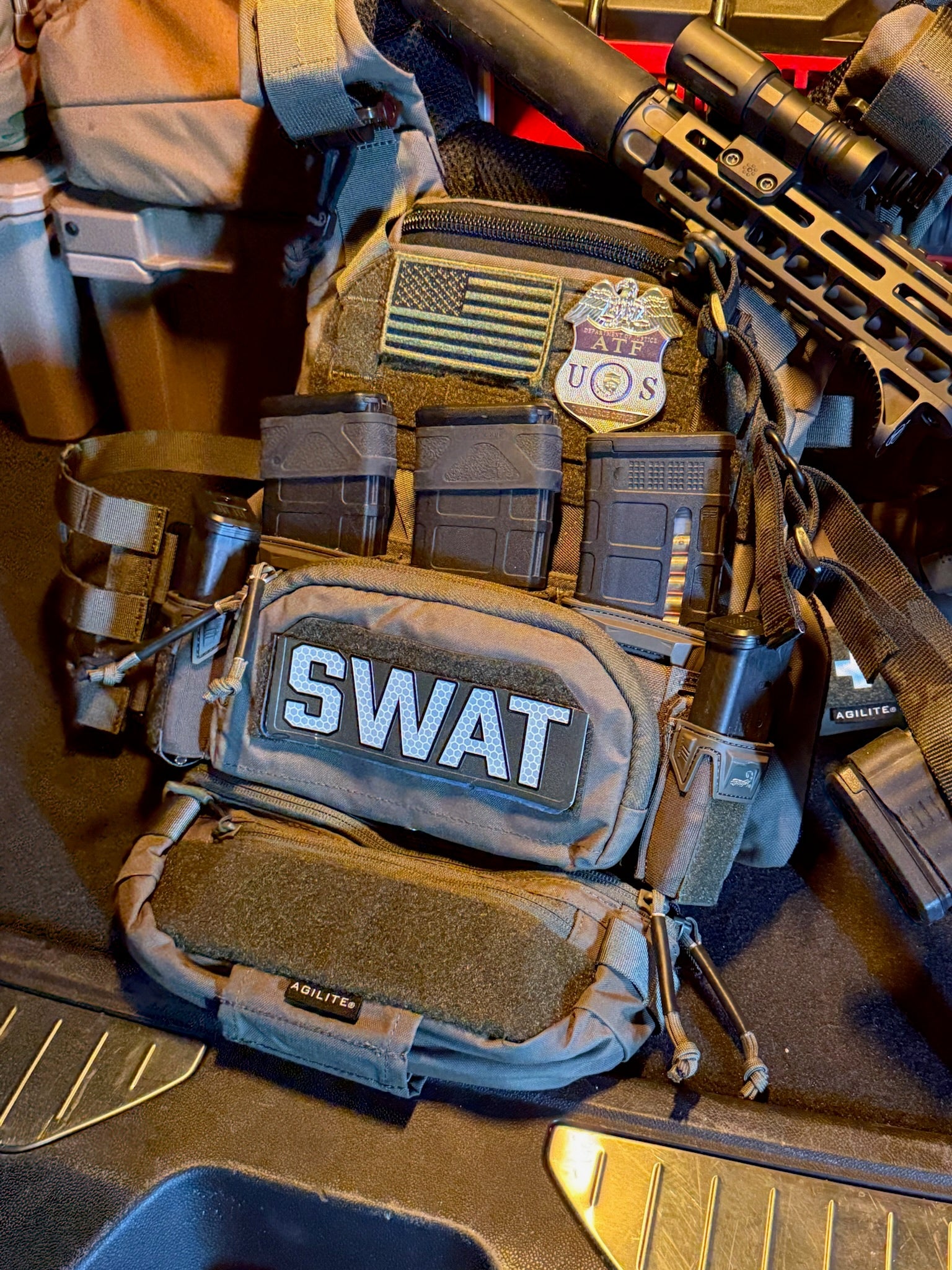 SWAT gear with tactical pouches and a rifle on a reflective surface with an ATF TFO Flex Badge patch. 