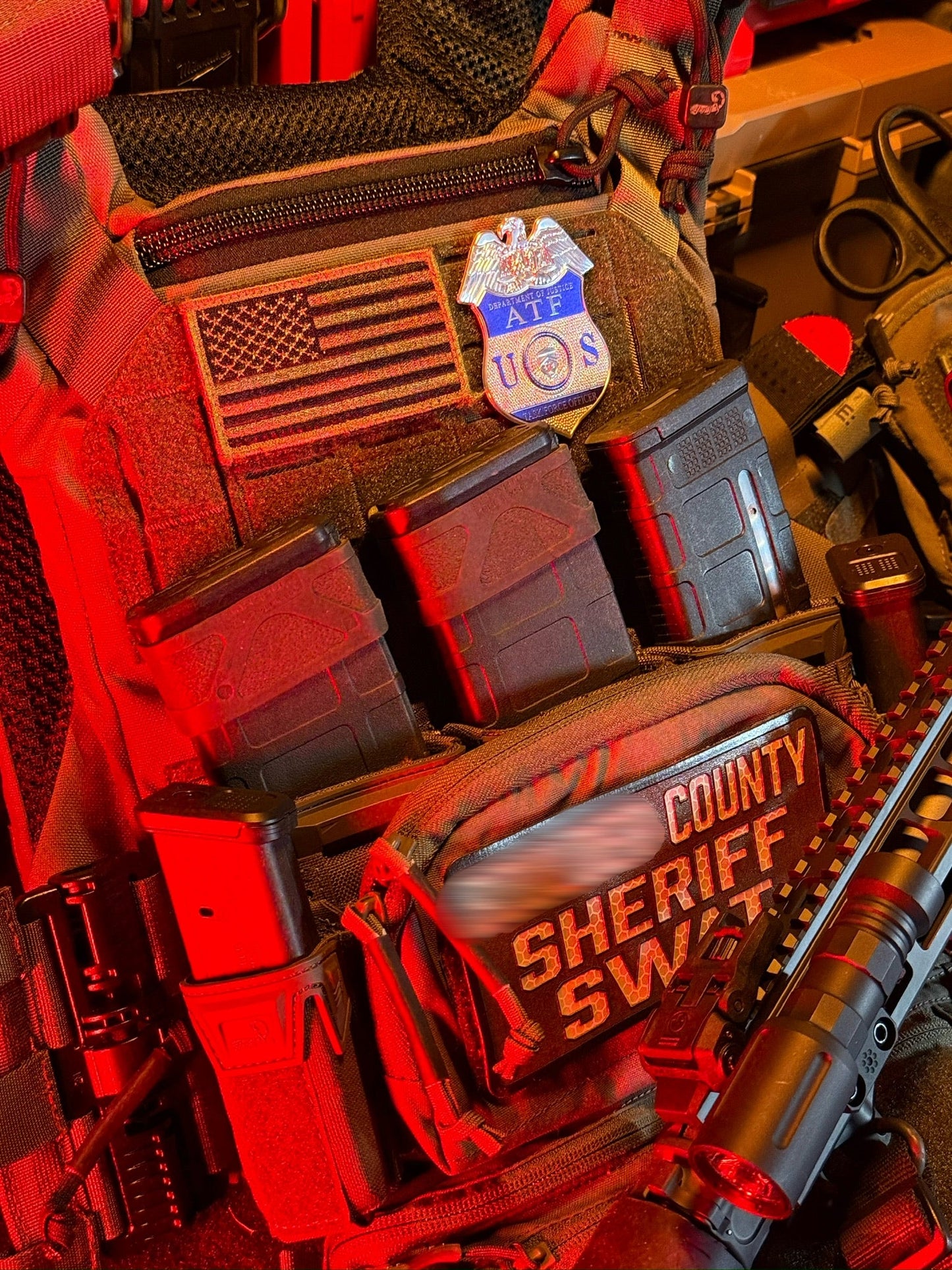 Close-up of a tactical vest with 'county Sheriff SWAT' text and American flag patch with ATF TFO Flex Shield Badge