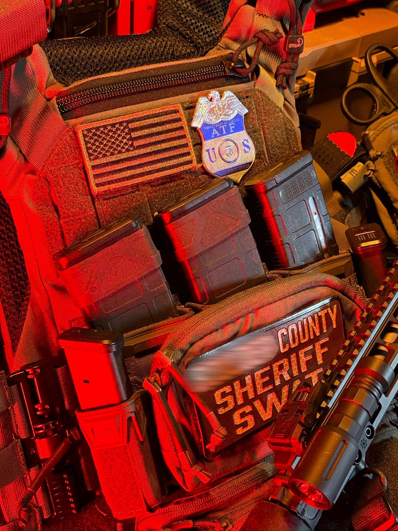 Close-up of a tactical vest with 'county Sheriff SWAT' text and American flag patch with ATF TFO Flex Shield Badge