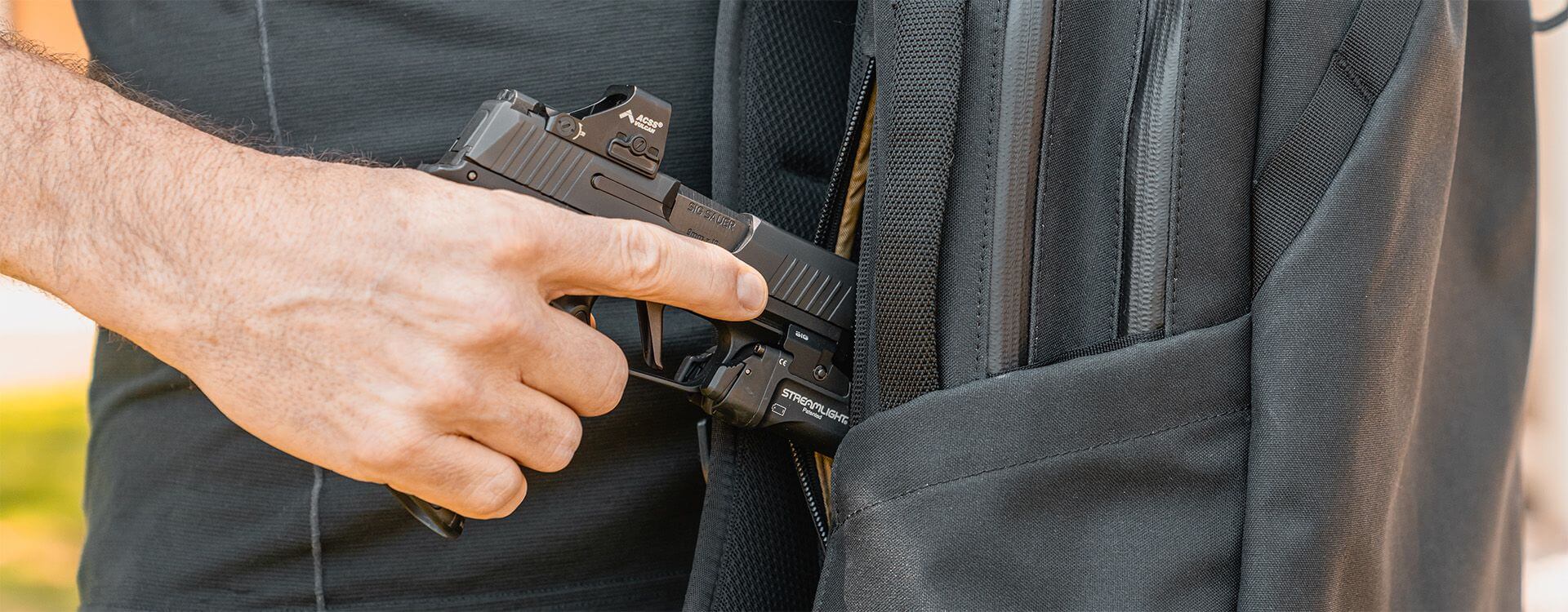 "Hand drawing a SIG Sauer pistol from the concealed carry compartment of the Magpul EDC25 Backpack, demonstrating tactical access and secure firearm storage
