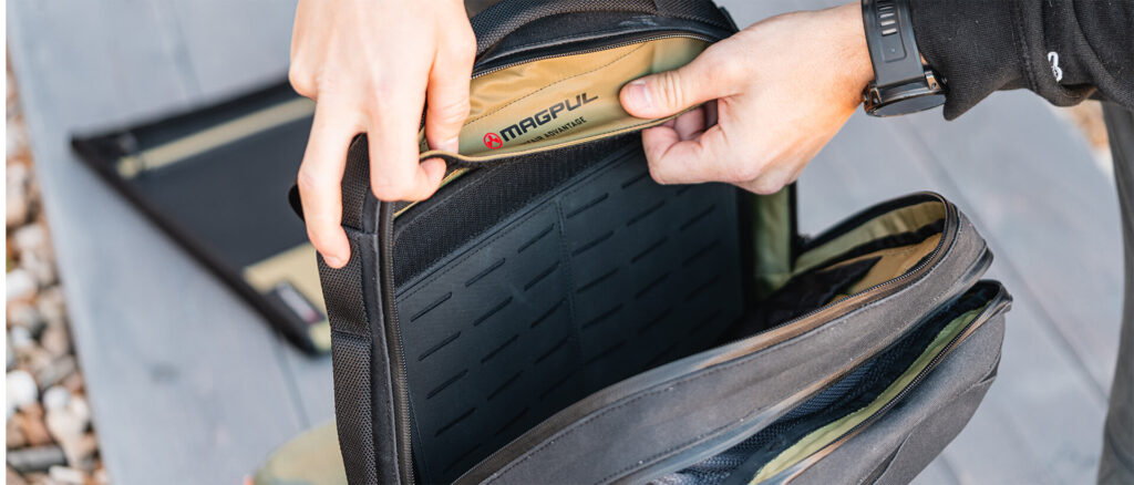 Hands installing the Magpul EDC Tactical Sleeve inside a backpack, showing MOLLE panel and hook-and-loop attachment system for modular loadout